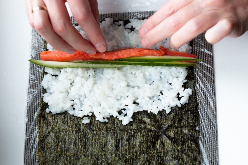 Woman sheet nori with rice puts cucumber red fish 326821 297